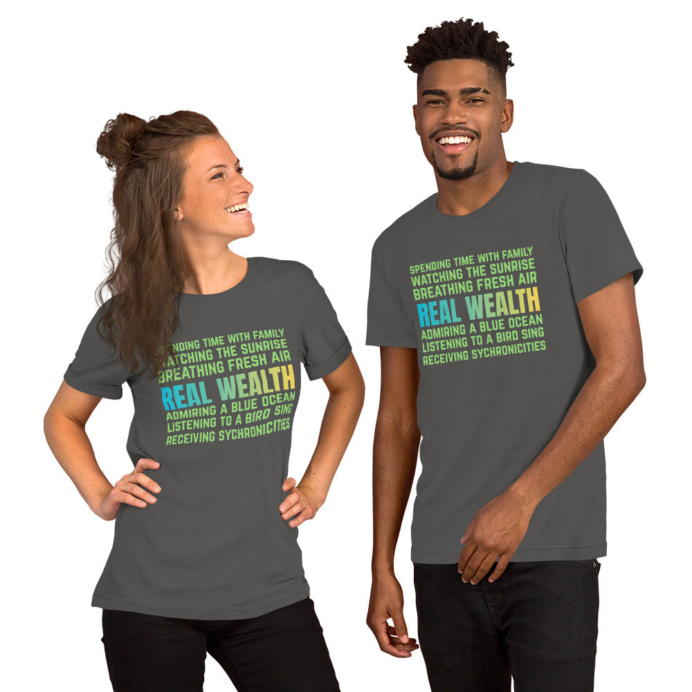 Dark grey unisex t-shirt featuring green and blue text reading “Real Wealth” with a list of lifestyle phrases.