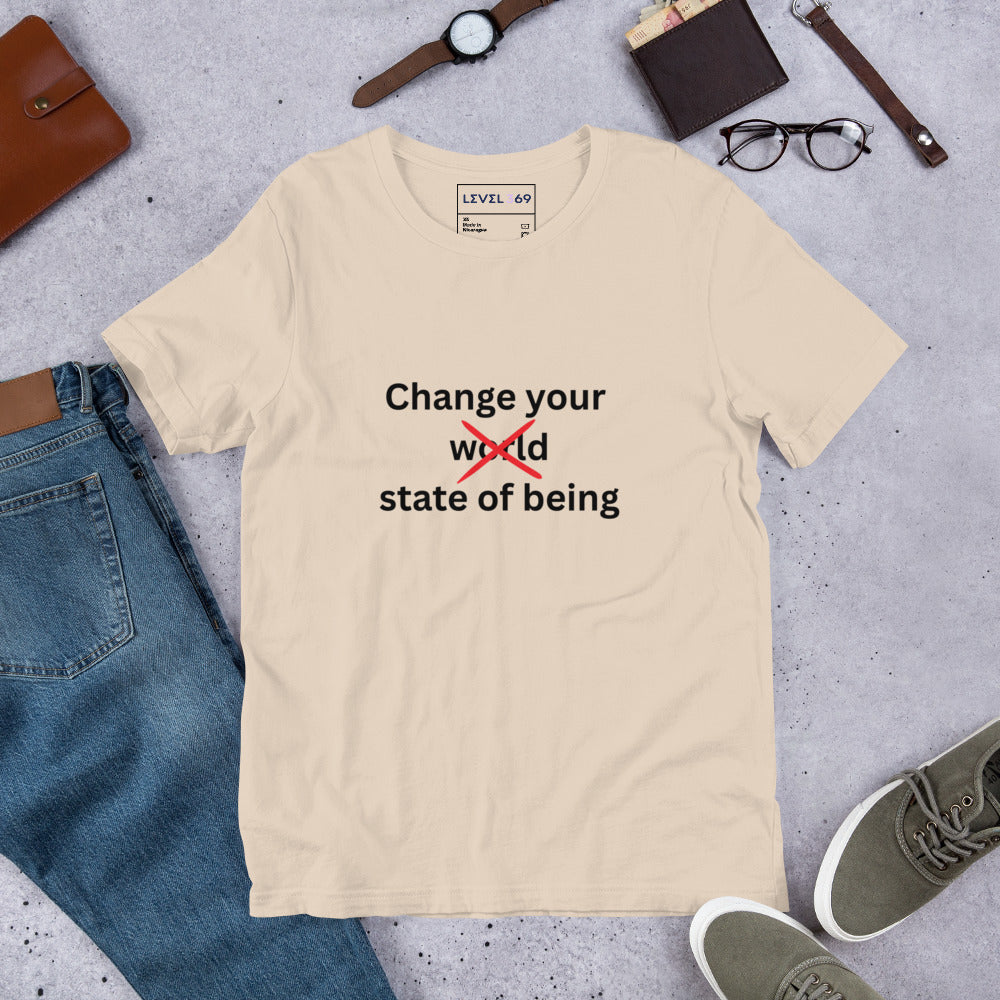 Cream minimalist t-shirt laid flat beside jeans, shoes, glasses, and accessories featuring the phrase “Change your state of being” with the word “world” crossed out in red typography.