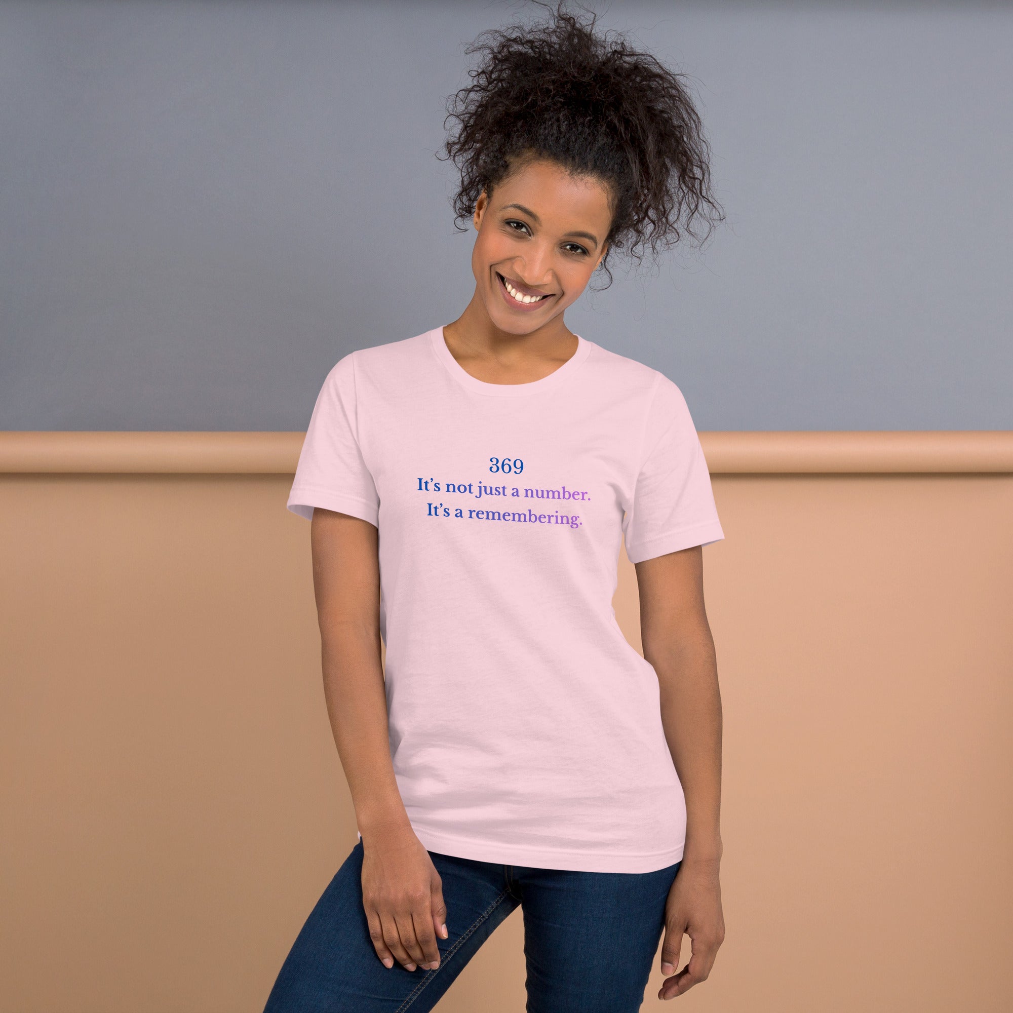 Model wearing a pink unisex t-shirt featuring the phrase ‘369 – It’s not just a number. It’s a remembering,’ in a soft blue-to-violet gradient.