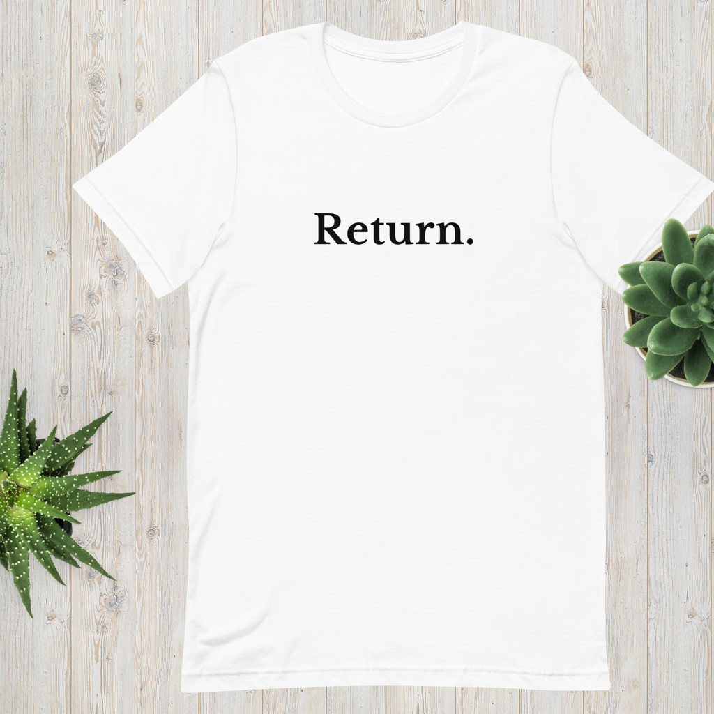 White “Return.” minimalist t-shirt displayed on a wooden surface with green plants for a calm, natural setting