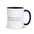 White ceramic mug with a blue interior and handle, featuring the phrase “369 is not a number. It’s a remembering.” in blue and lavender text.