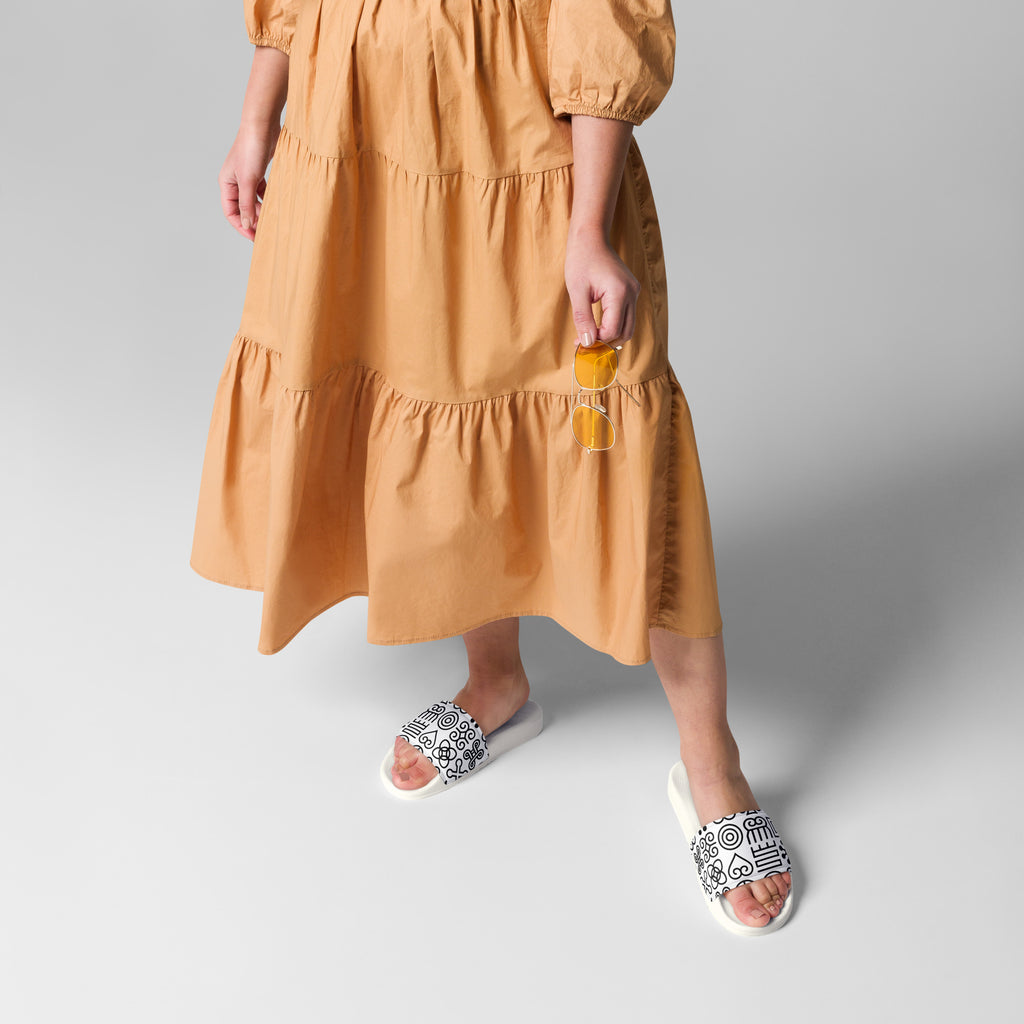 Woman wearing Adinkra symbol slides with an orange dress, showcasing conscious style, cultural expression, and effortless everyday wear
